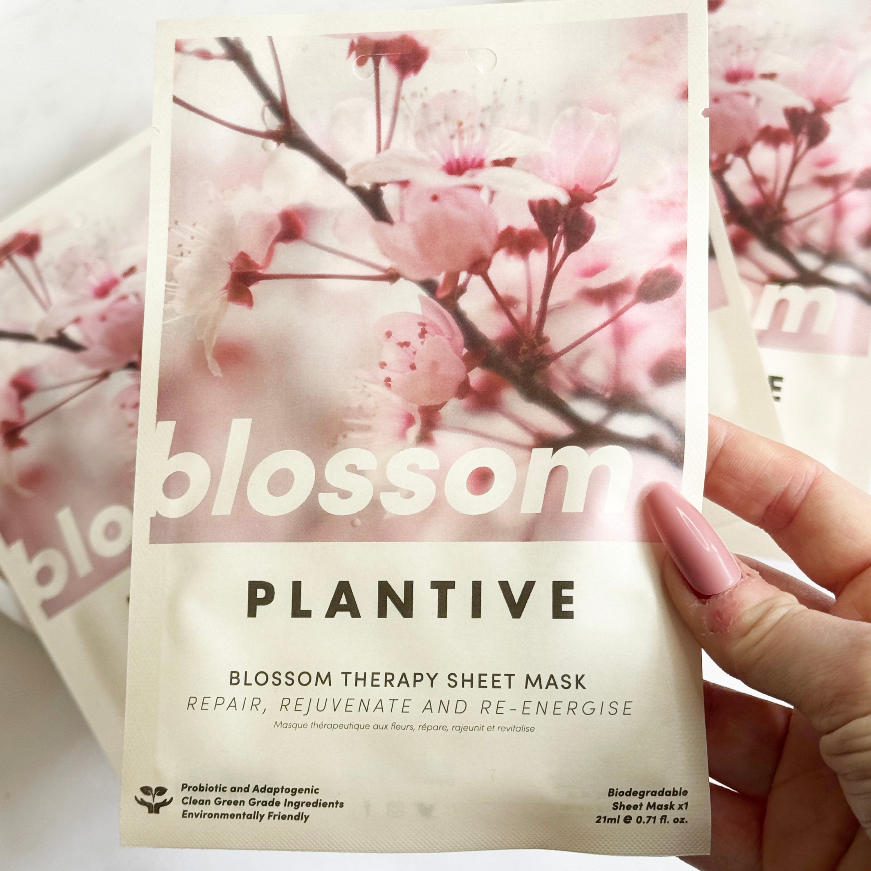 Plantive Blossom Therapy Sheet Mask packaging held by a hand with a cherry blossom background