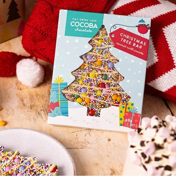 Christmas-themed table setting with a tree-shaped cookie, hot chocolate, and gift boxes.