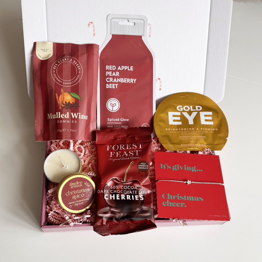 Assorted Christmas-themed products including sweet treats, a candle, and skin care in a postal box on a white background.