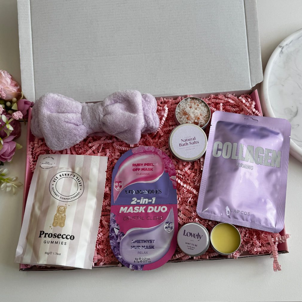 Lilac-themed pamper gift box including a fluffy headband, collagen sheet mask, bath salts, face mask duo, Prosecco gummies, mint lip balm and lavender tin candle.