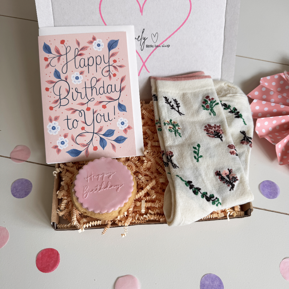 Gift set with a card, cookie, and socks on a white surface with heart designs.