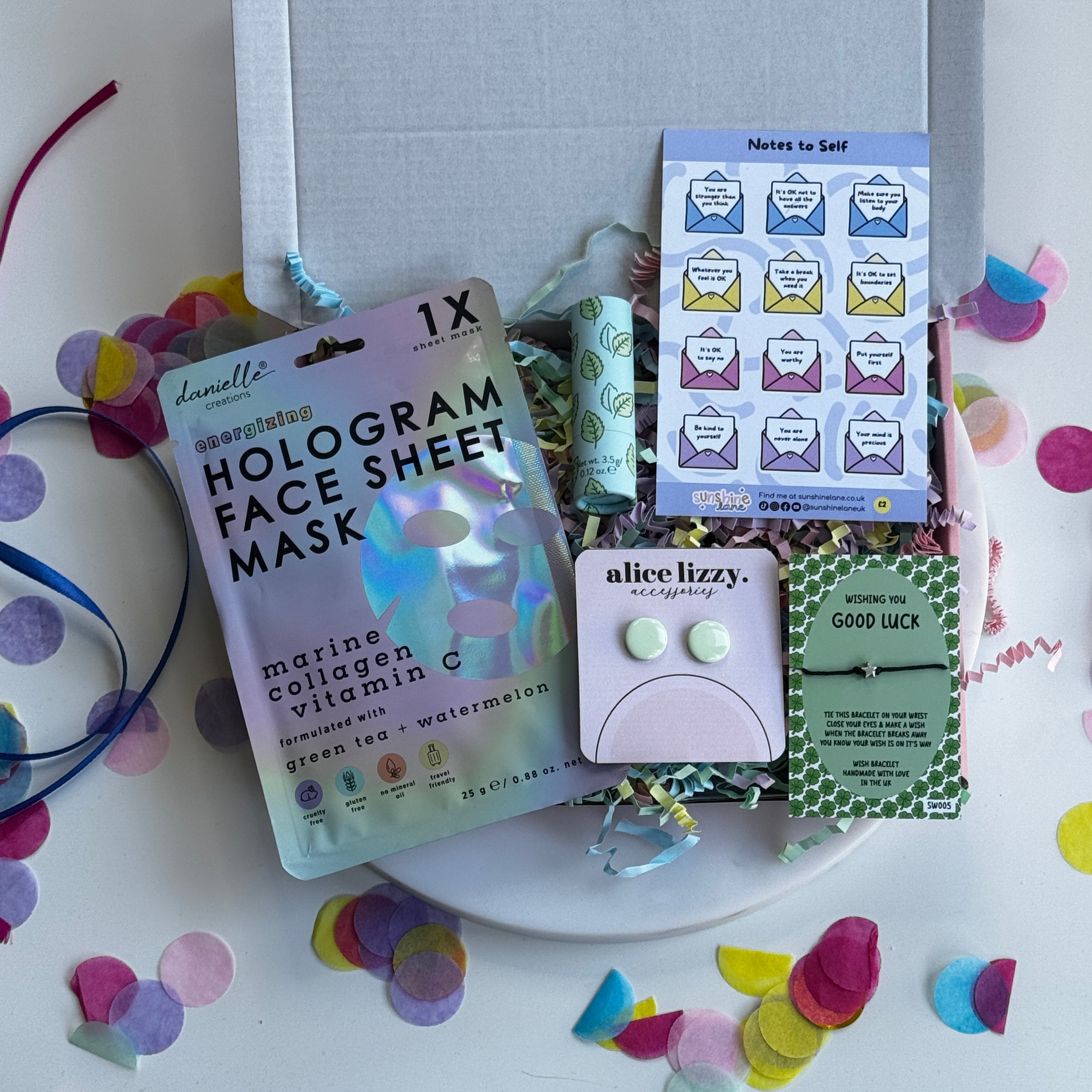 Flat lay of a pink self-care gift box with pamper treats, skincare items, and soft-toned packaging designed for relaxation and gifting.