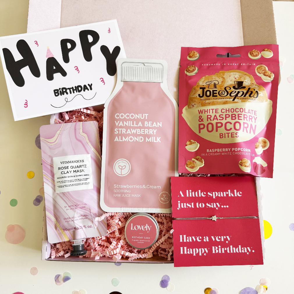 Birthday gift set with coconut vanilla strawberry almond milk, hand mask, and popcorn bites on a light pink background.