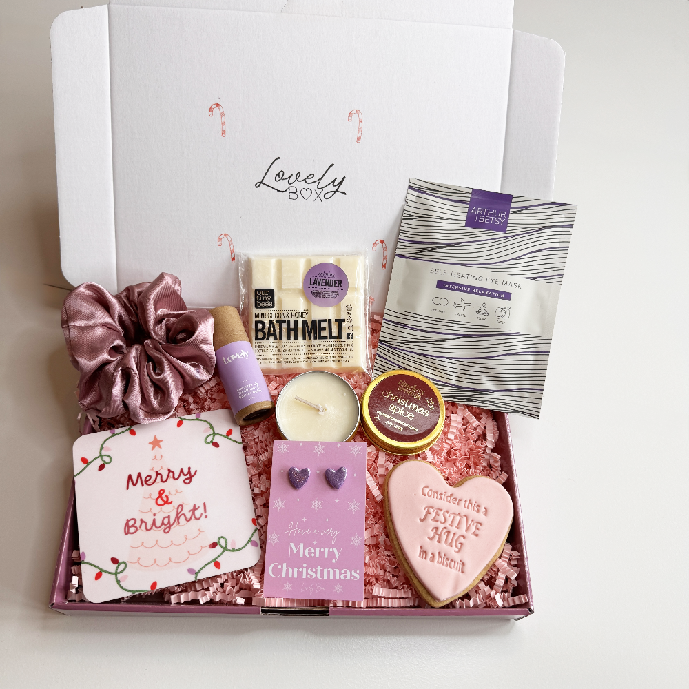 Gifting box with various items including a candle, card, and bath melt on a white background