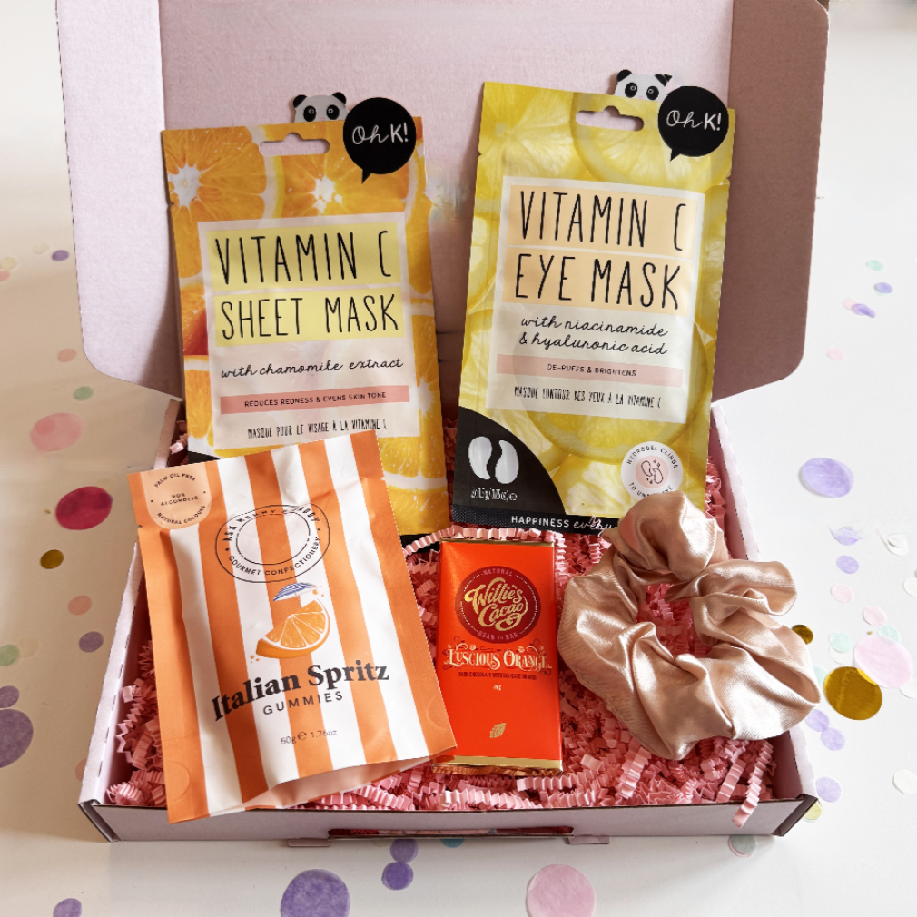 Box containing skincare products, gummies, and a scrunchie on a colorful confetti background