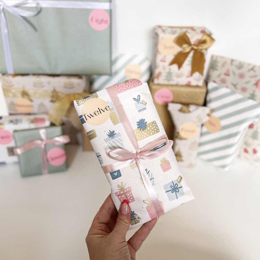 Hand holding a decorated gift box with a festive design, surrounded by other wrapped gifts.