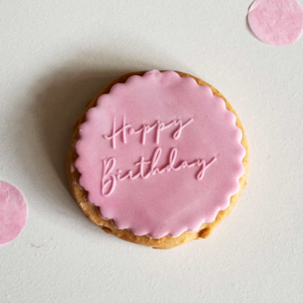Cookie with pink icing and 'Happy Birthday' text on a light background
