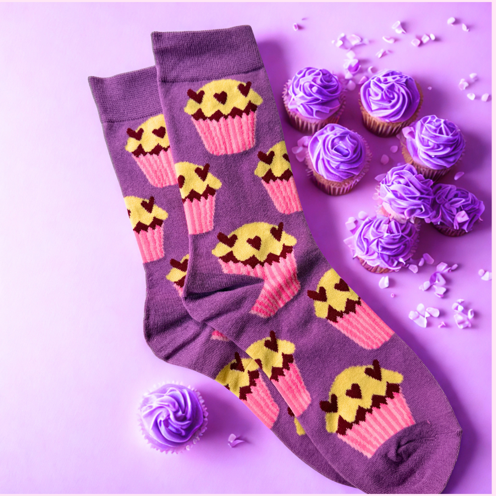 Purple socks with cupcake pattern next to cupcakes on a purple background