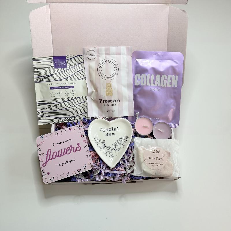 Gift box with various items including a card, heart-shaped ornament, and packets on a white background