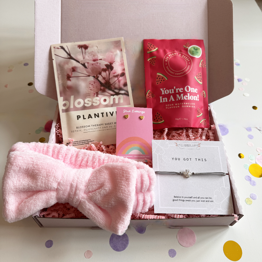 Pink self-care and encouragement gift box with blossom sheet mask, watermelon vegan sweets, You Got This bracelet, pink bow headband, and rainbow stud earrings.