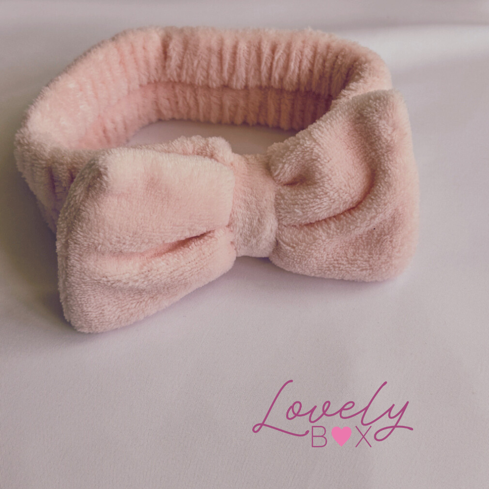 Pink fuzzy headband with a bow on a light gray background, featuring the brand 'Lovely Box'.