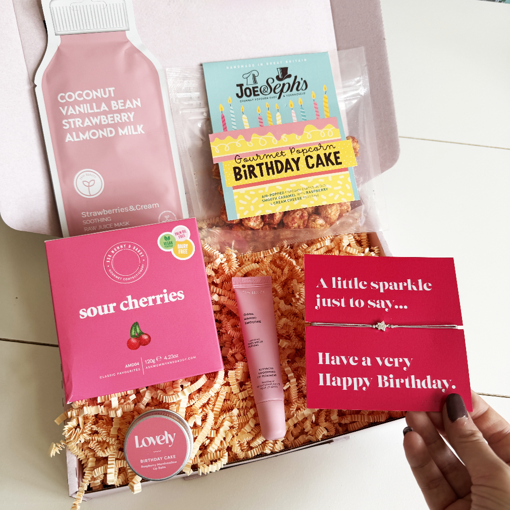 Gift box with coconut vanilla strawberry almond milk, Joe Sephs birthday cake popcorn, sour cherries candy, and a bracelet.