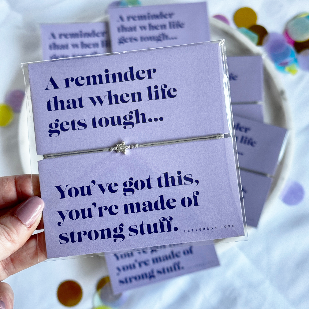 Purple card with a message and a silver bracelet, held by a hand.