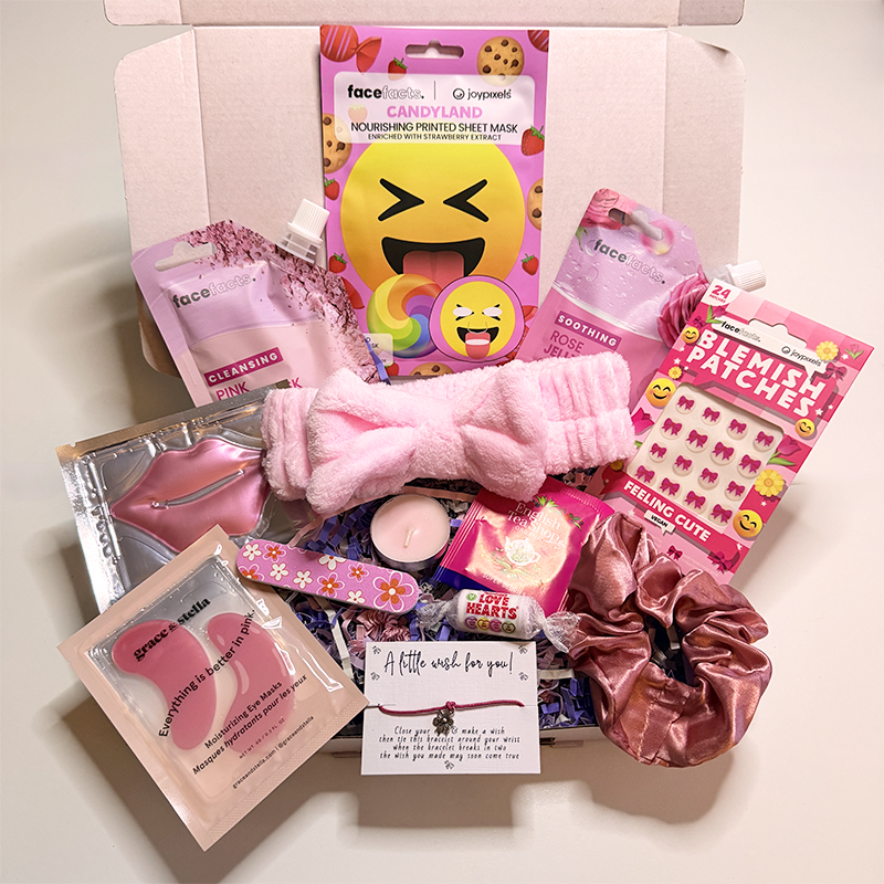 Open pink gift box filled with teen pamper and skincare treats including colourful face masks, blemish patches, pink scrunchies, beauty accessories, tea, sweets and a fluffy spa headband arranged neatly inside pastel packaging.