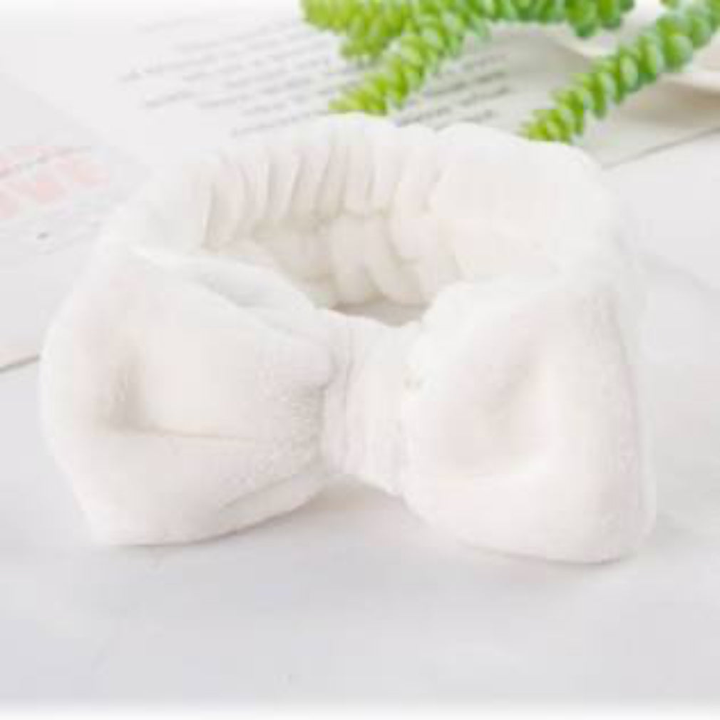 White plush bow toy on a light background with green leaves.