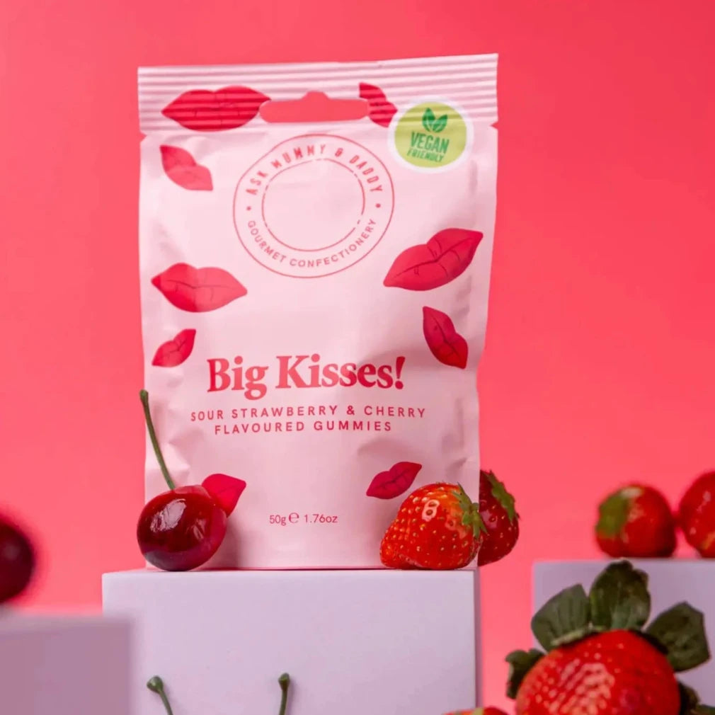 Packaging of Big Kisses gummies with strawberries and cherries on a pink background