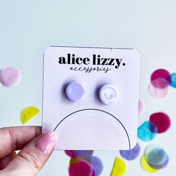 Earring card with purple and white earrings held by a hand against a colorful confetti background