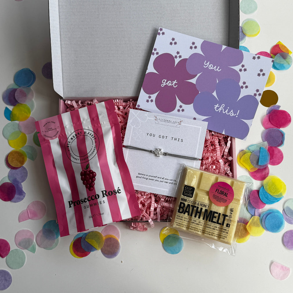 Motivational gift box with pink Prosecco Rosé gummies, mini cocoa & honey bath melt, “You Got This” floral card, and wish bracelet with silver star charm, surrounded by colourful confetti.
