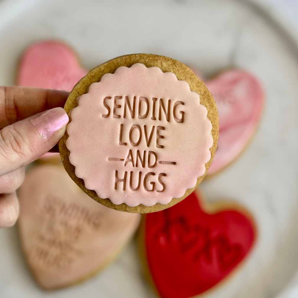 Handmade biscuit with fondant icing. circle shaped with the words sending love and hugs